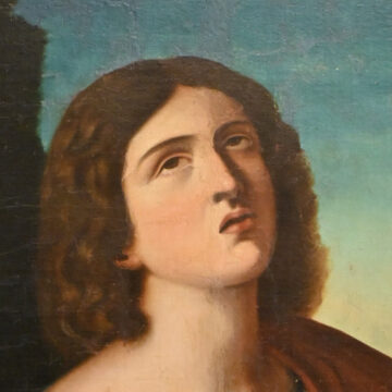 Pintura religiosa de San Juan Bautista con cruz de caña y túnica roja sobre fondo de paisaje, enmarcada en madera tallada.