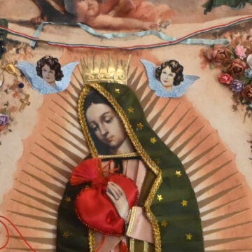 Obra religiosa de la Virgen de Guadalupe con manto verde, aureola radiante y decoraciones aplicadas de flores y corazón.