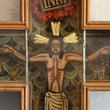 Cruz devocional de madera con representación de Cristo crucificado, inscripción INRI y motivos florales en tonos dorados y rojos.