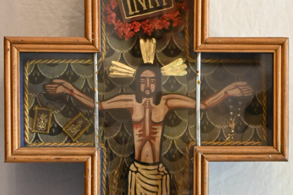 Cruz devocional de madera con representación de Cristo crucificado, inscripción INRI y motivos florales en tonos dorados y rojos.