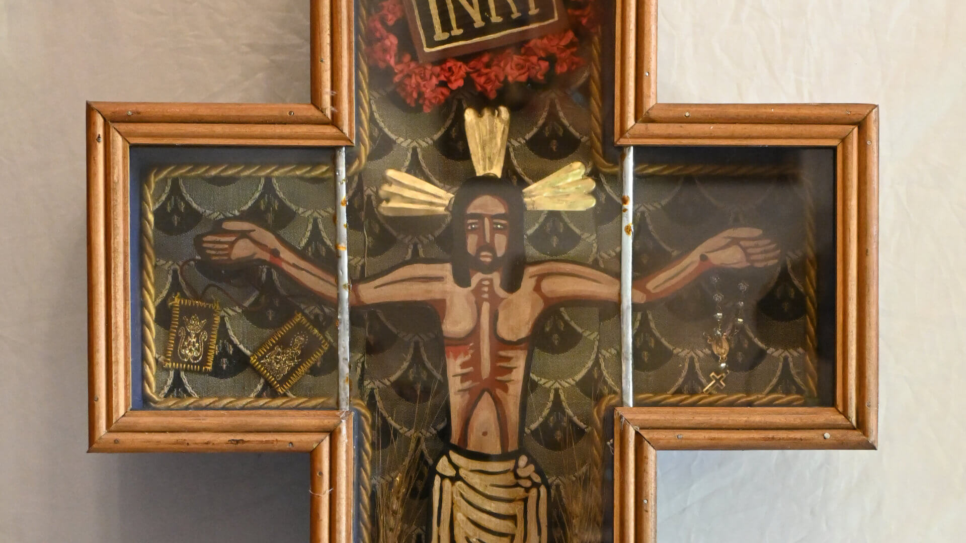 Cruz devocional de madera con representación de Cristo crucificado, inscripción INRI y motivos florales en tonos dorados y rojos.